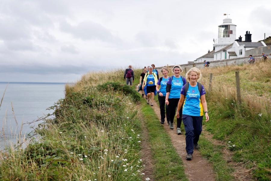 A line of trekkers walking on a costal path with a lighthouse